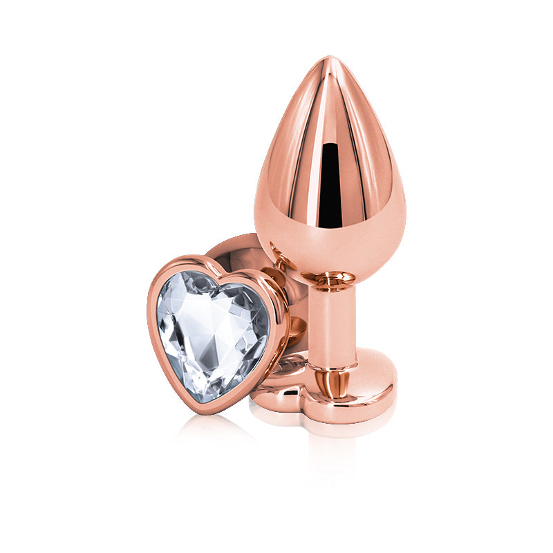 Close-up photo shows the Rear Assets Heart Anal Plug w/ Gem (rose gold/clear) from NS Novelties, shows its long neck for comfort as well as its faceted heart-shaped gem.