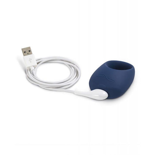 Image shows the cock ring laying on its side with the magnetic USB charging cord attached to it.