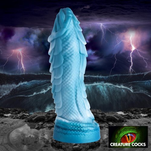 Sci-fi/fantasy image of the Scaly dildo on a dark rocky piece of land with rough, dark water, waves crashing up. The sky is an ominous black and blue with purple bolts of lightning. The bottom right-hand corner has a small logo image for Creature Cocks that is a close-up eye of a monster. 