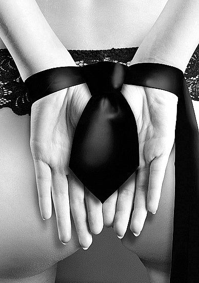 Black and white photo of the back of a woman with her hands bound by the black satin bondage tie.